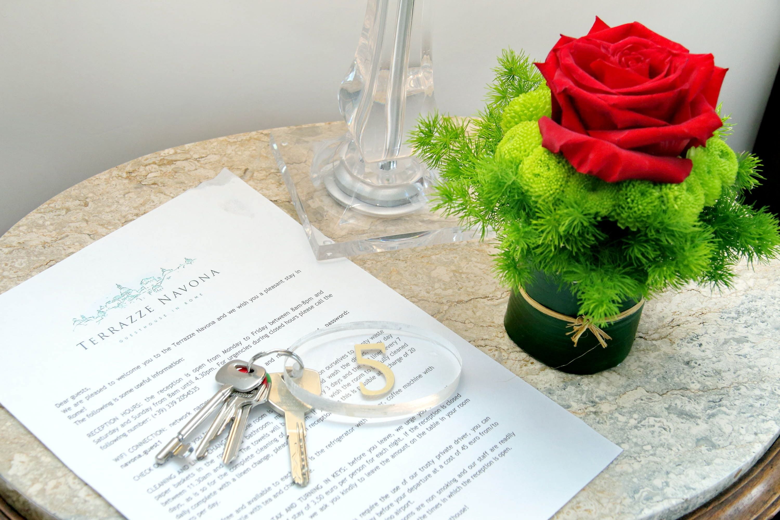 A document titled "TERRAZZE NAVONA" with keys and a red rose on a marble surface.