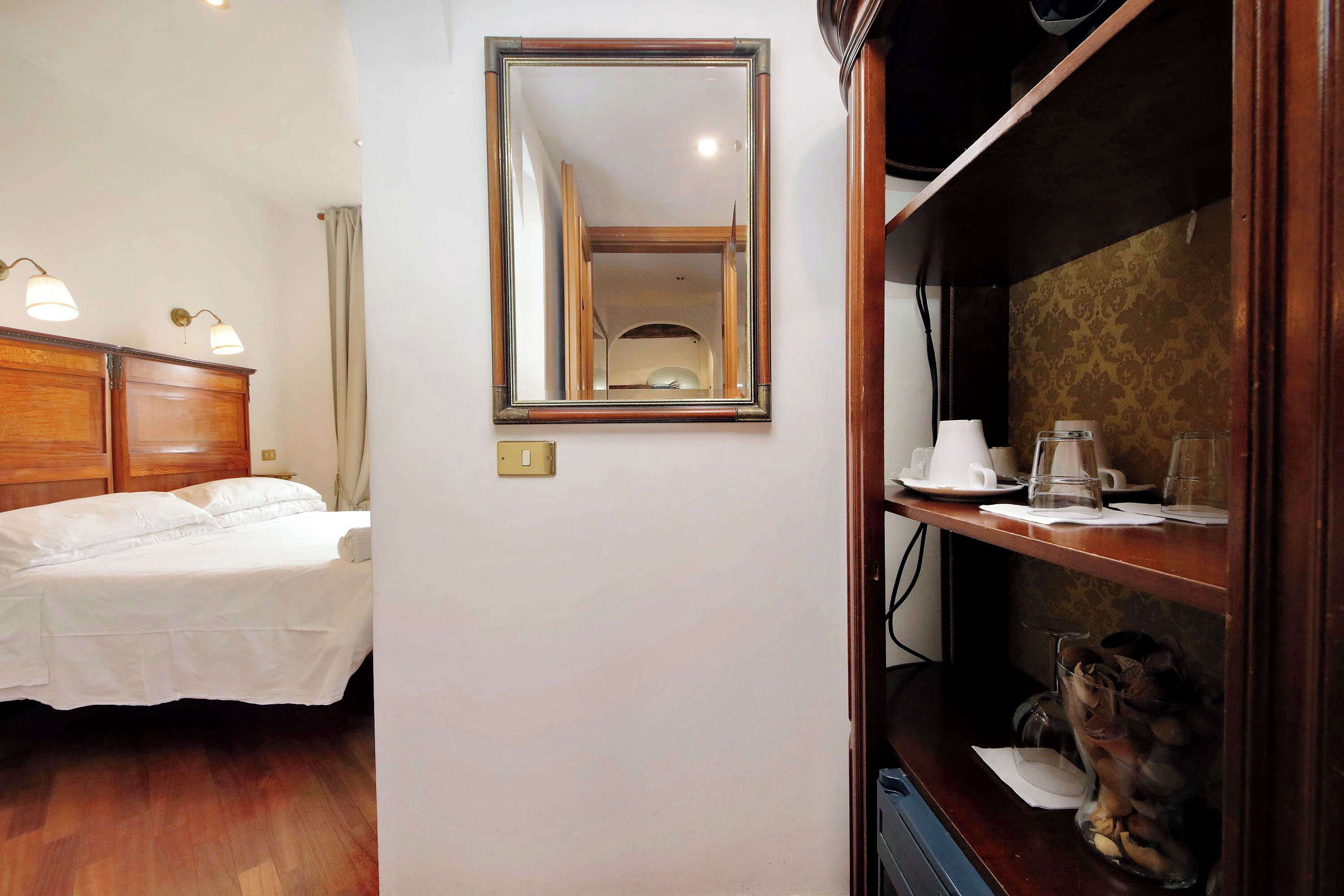 Une chambre d’hôtel équipée d’un lit, d’un miroir, d’une étagère avec une machine à café et d’un vase décoratif.
