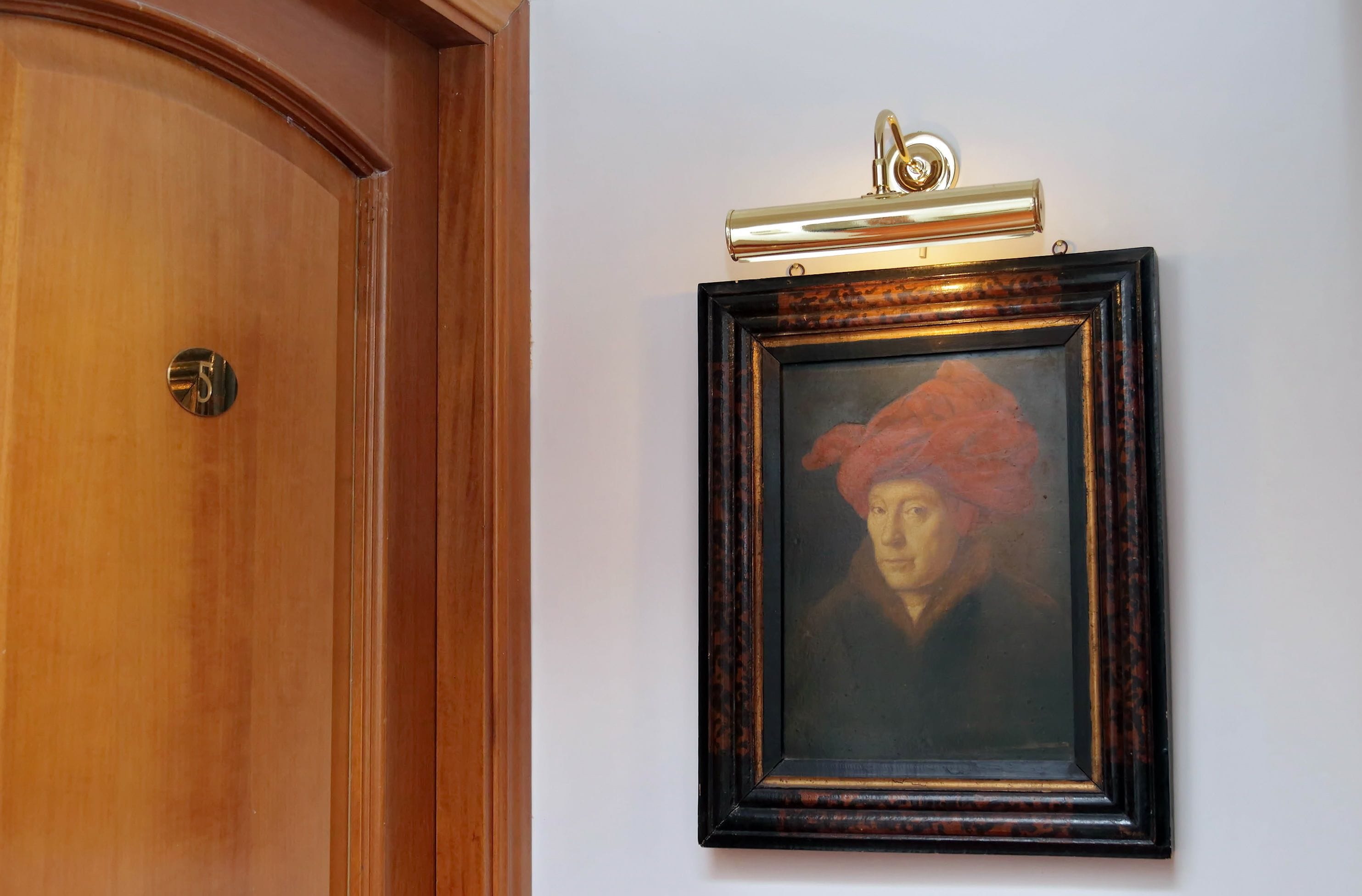Una puerta de madera con un picaporte de latón y un cuadro en la pared que muestra un pañuelo rojo.