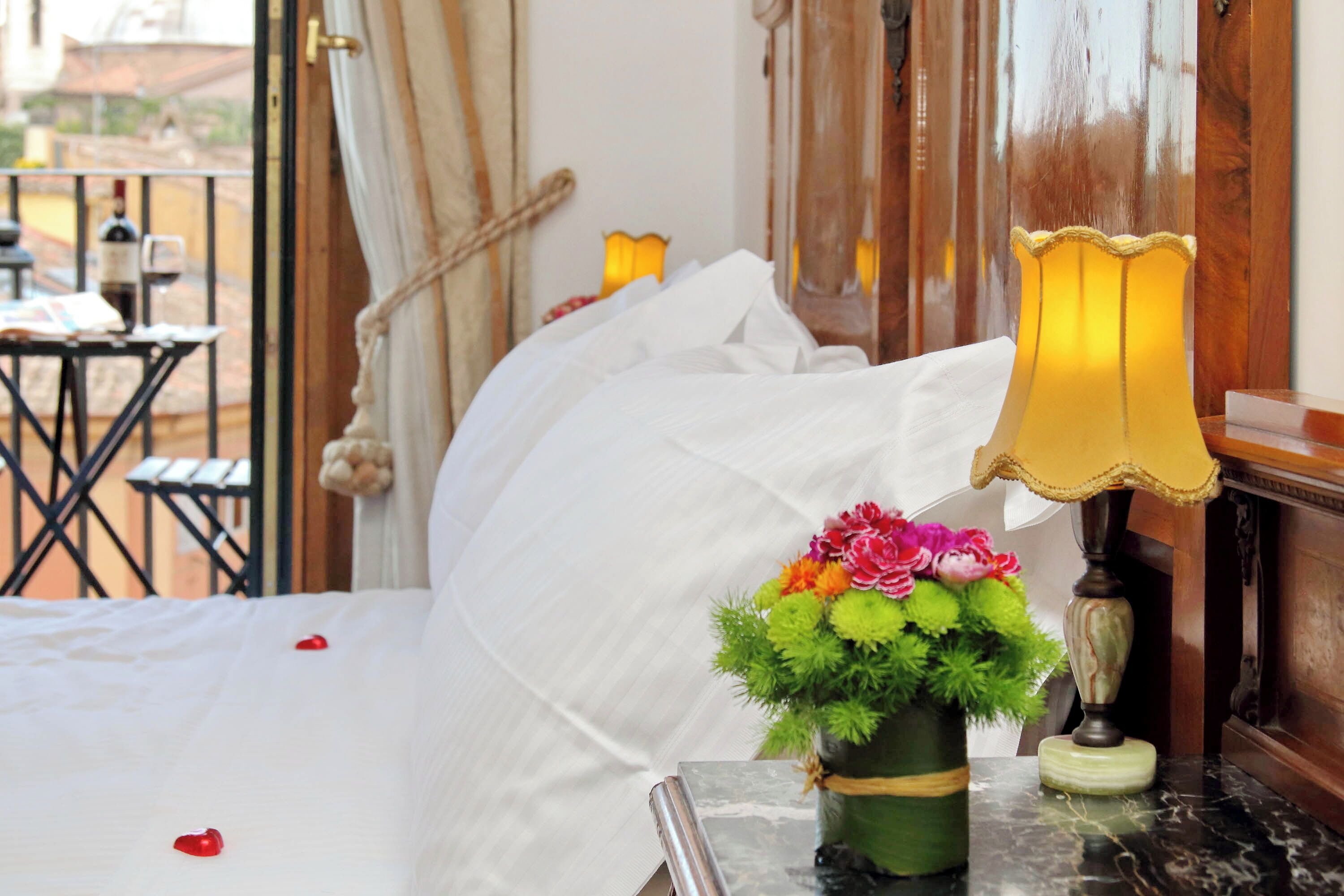 A hotel room with a bed, a small table with a vase of flowers, and a lamp.