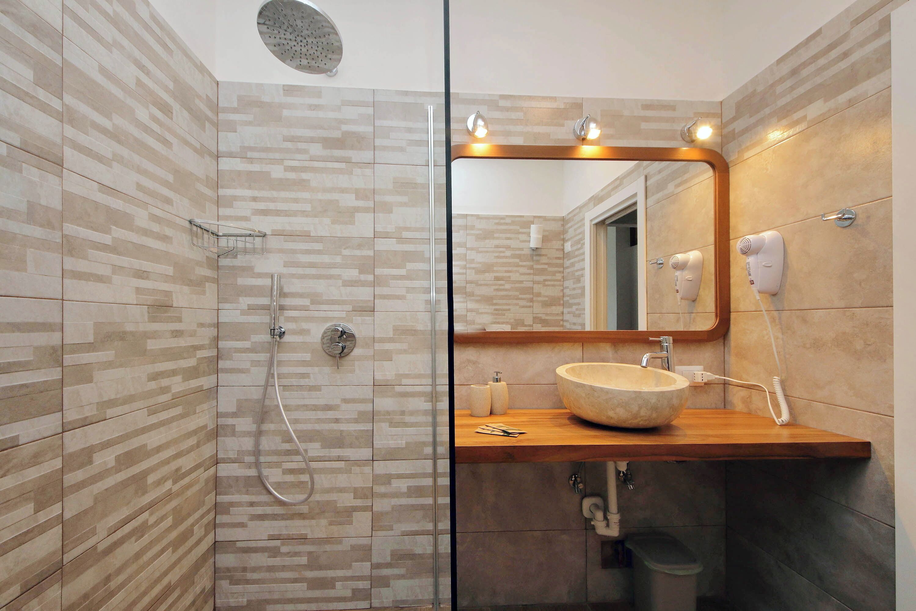 A bathroom with a shower, a sink with a large bowl, a mirror, and a hairdryer.
