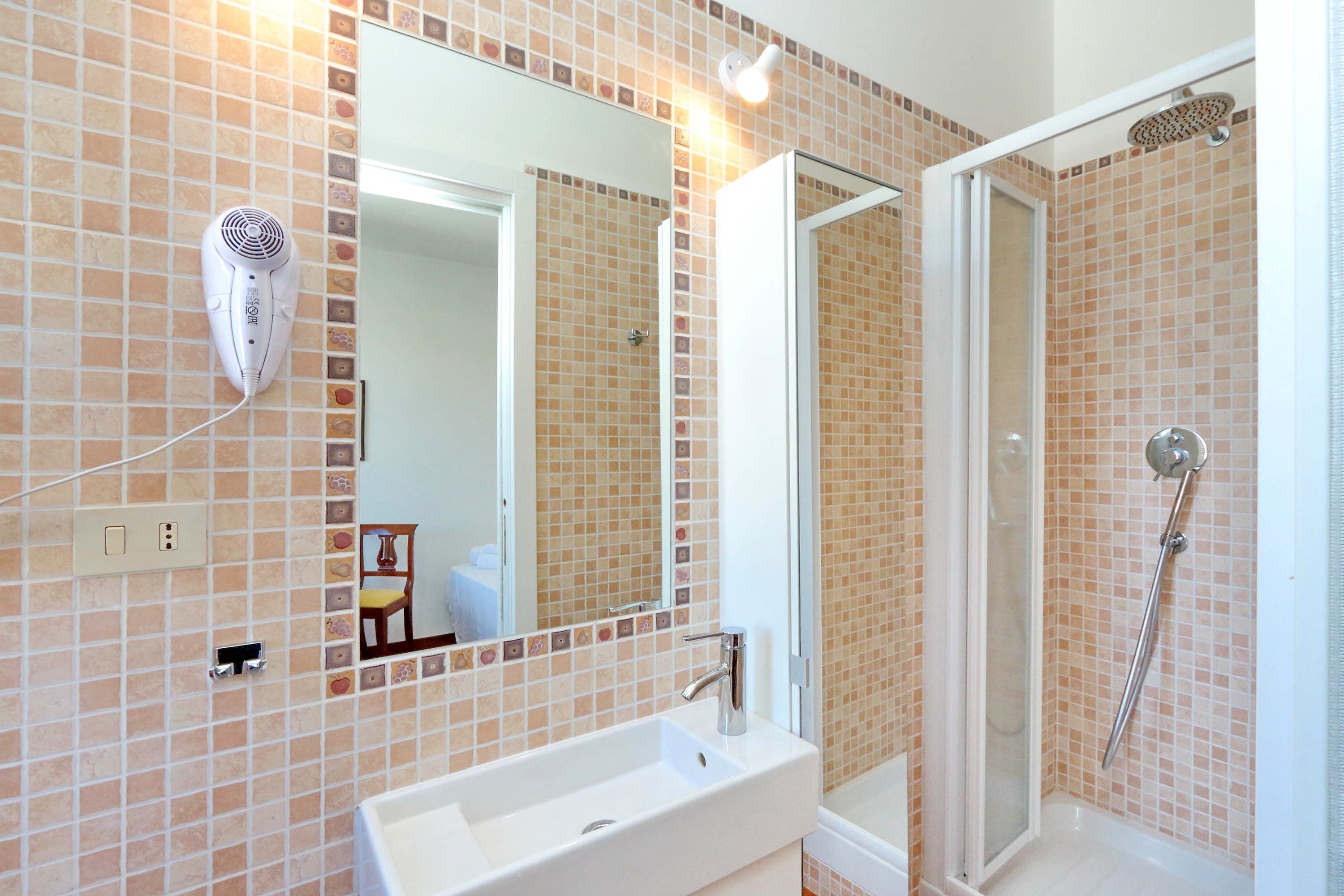 A bathroom with a white sink, a mirror, a hairdryer mounted on the wall, and a shower area.