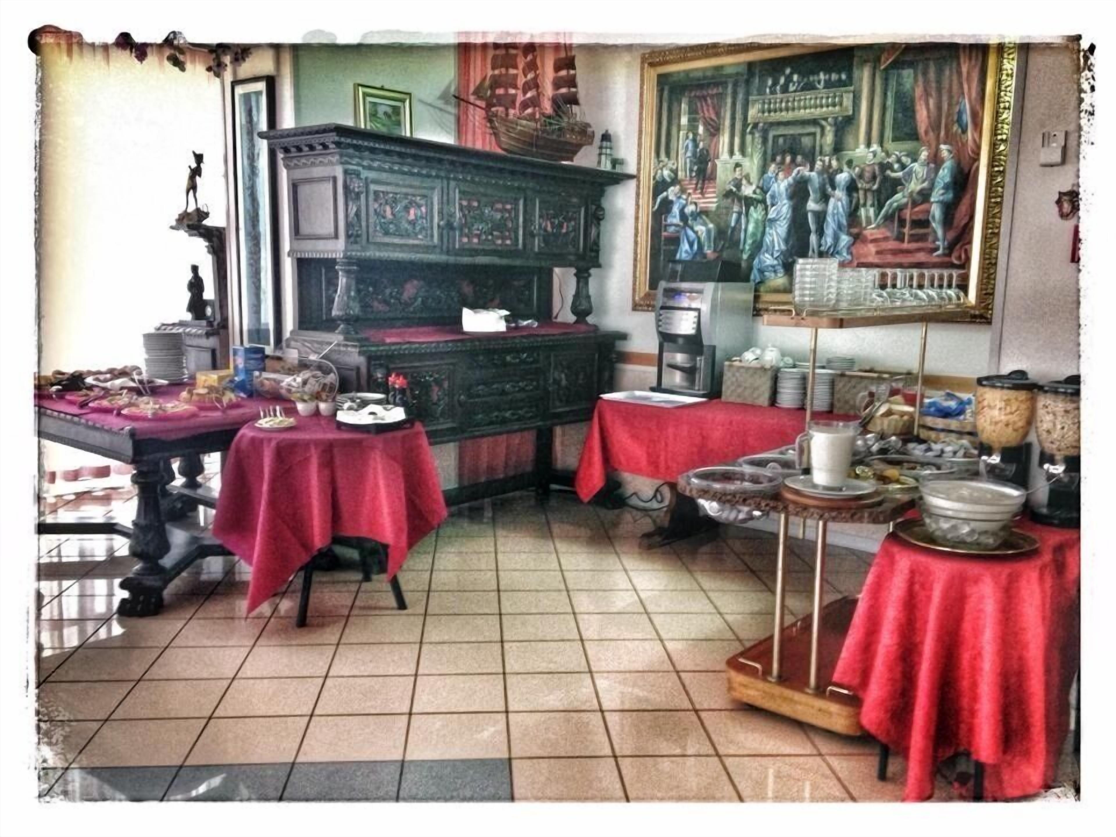 A room with a dining table set for a meal, a coffee machine, and a painting on the wall.