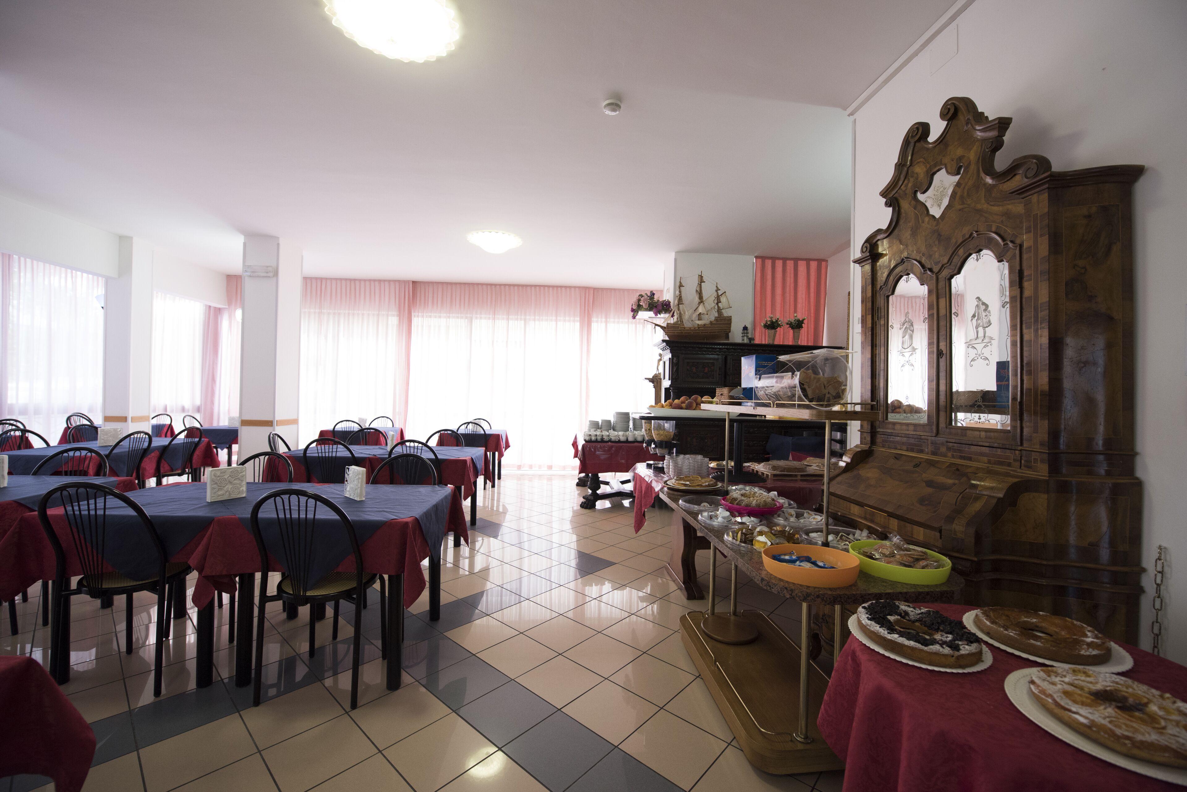 A dining area with multiple tables and chairs, a buffet table with various dishes, and a decorative wooden cabinet.