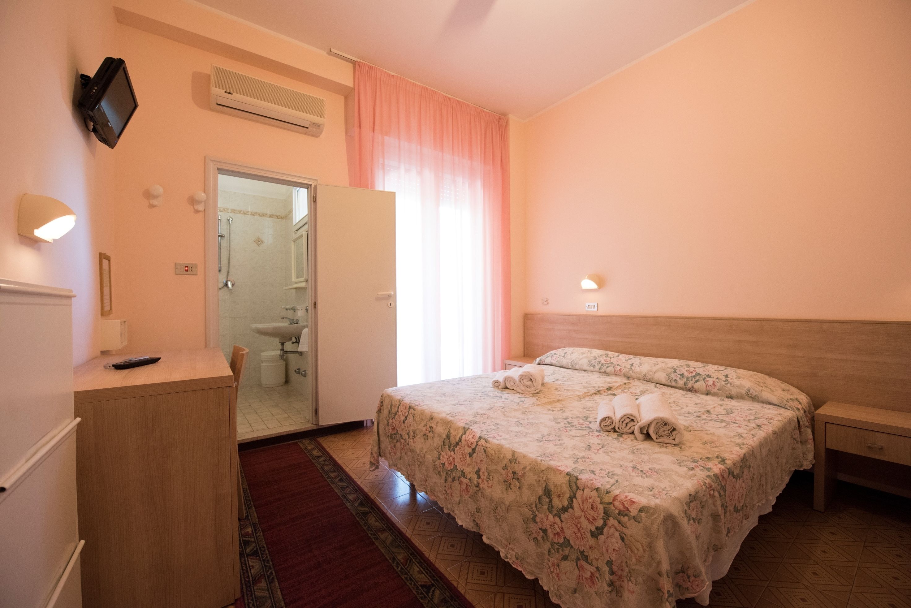 Habitación de hotel con cama, escritorio, espejo, lavabo y ducha.