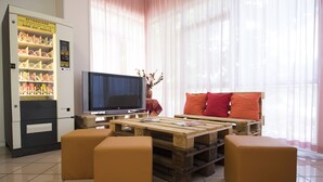 Una sala de estar con televisor, mesa de centro de palets de madera y otomanas naranjas.