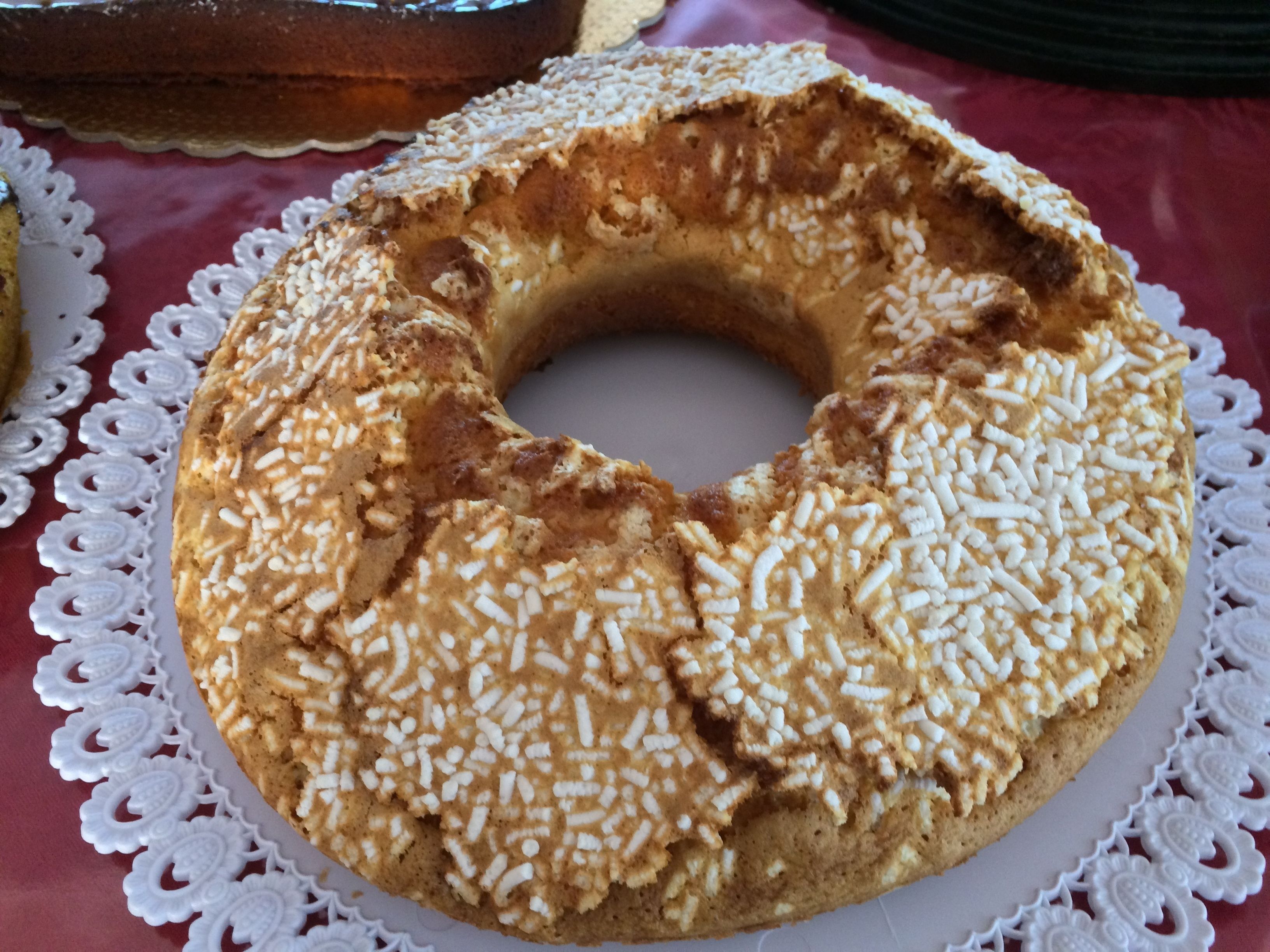 A round cake with white sprinkles on a white plate, placed on a lace doily.