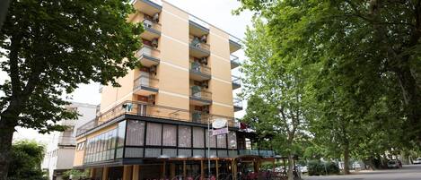 A multi-story hotel with balconies, a ground-level restaurant with outdoor seating, and a street view.
