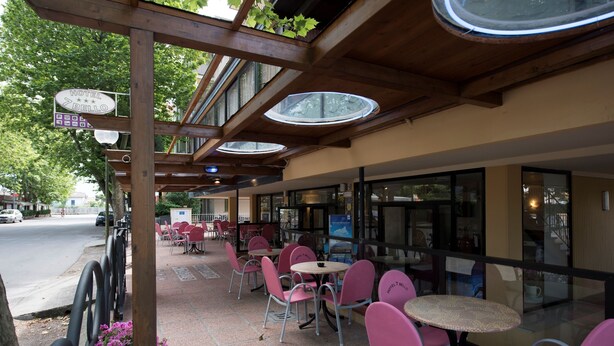 Un patio de hotel con mobiliario exterior, una pérgola de madera y vista a la calle.