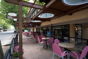 A hotel patio with outdoor seating, a wooden pergola, and a street view. - Hotel Settebello (Cesenatico)