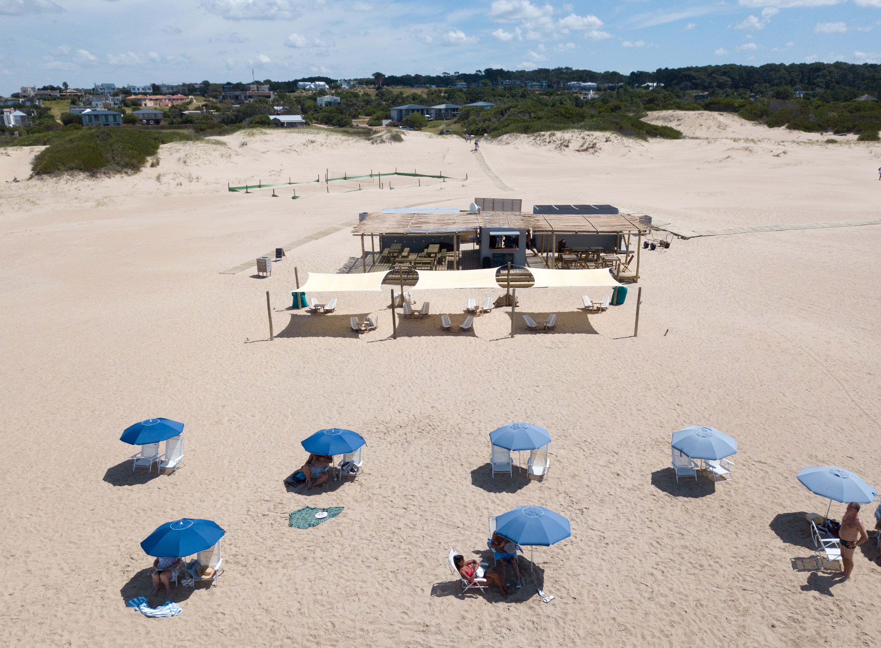 Un resort frente a la playa con múltiples sombrillas, sillas de descanso y un edificio central con terraza.