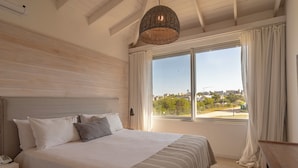 A bedroom with a large bed, a bedside table with a phone, a window with curtains, and a view of the city.
