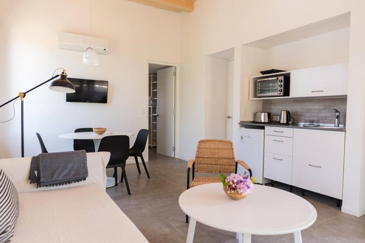 A compact living space with a kitchenette, a dining area with a table and chairs, and a sofa with a blanket.