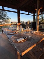 A wooden dining table set with placemats, wine glasses, and cutlery, overlooking a scenic landscape.