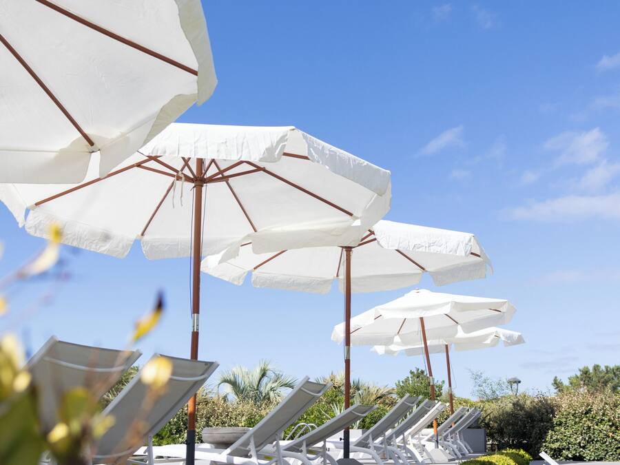 A row of white sun loungers with umbrellas, set against a clear blue sky.