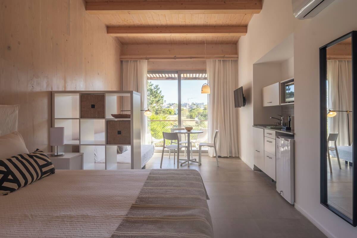 A bedroom with a large bed, a bedside table, a built-in shelving unit, and a view of the outdoors through a sliding door.
