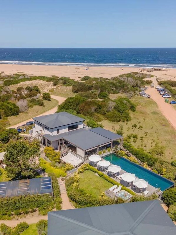 A beachfront property with a swimming pool, solar panels, and a view of the ocean.