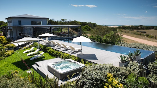 A modern house with a large swimming pool, sun loungers, and a hot tub.