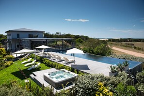 Una casa moderna con una gran piscina, tumbonas y un jacuzzi.