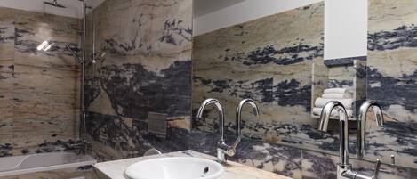 A modern bathroom with marble walls, a bathtub, two sinks, and a glass shower enclosure.