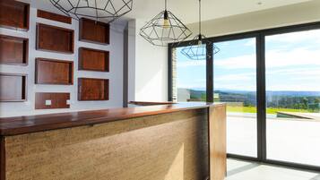 A modern reception area with a wooden reception desk, geometric pendant lighting, and a large glass door leading to an outdoor view.