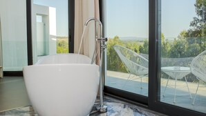 A modern bathroom with a large white bathtub, a shower, and a view of a balcony with outdoor furniture. - Enigma - Nature & Water Hotel (Odemira)