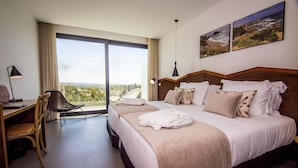 A hotel room with a large bed, a desk, a chair, and a view of the outdoors. - Enigma - Nature & Water Hotel (Odemira)