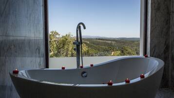 A freestanding bathtub with candles, a faucet, and a view of a landscape through a window.
