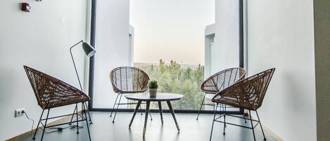 Una habitación moderna con un ventanal grande, dos sillas de mimbre, una mesita y una planta en maceta.