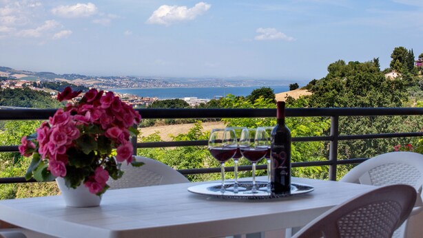 Una mesa con un jarrón de flores y copas de vino en un balcón con vistas a un paisaje costero.
