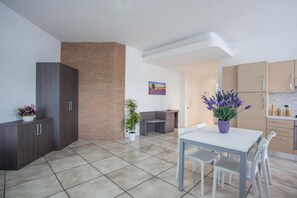 A modern kitchen with light wood cabinets, a dining area with a white table and chairs, and a small seating area with a bench and potted plants. - Fiori Del Conero (Ancona)