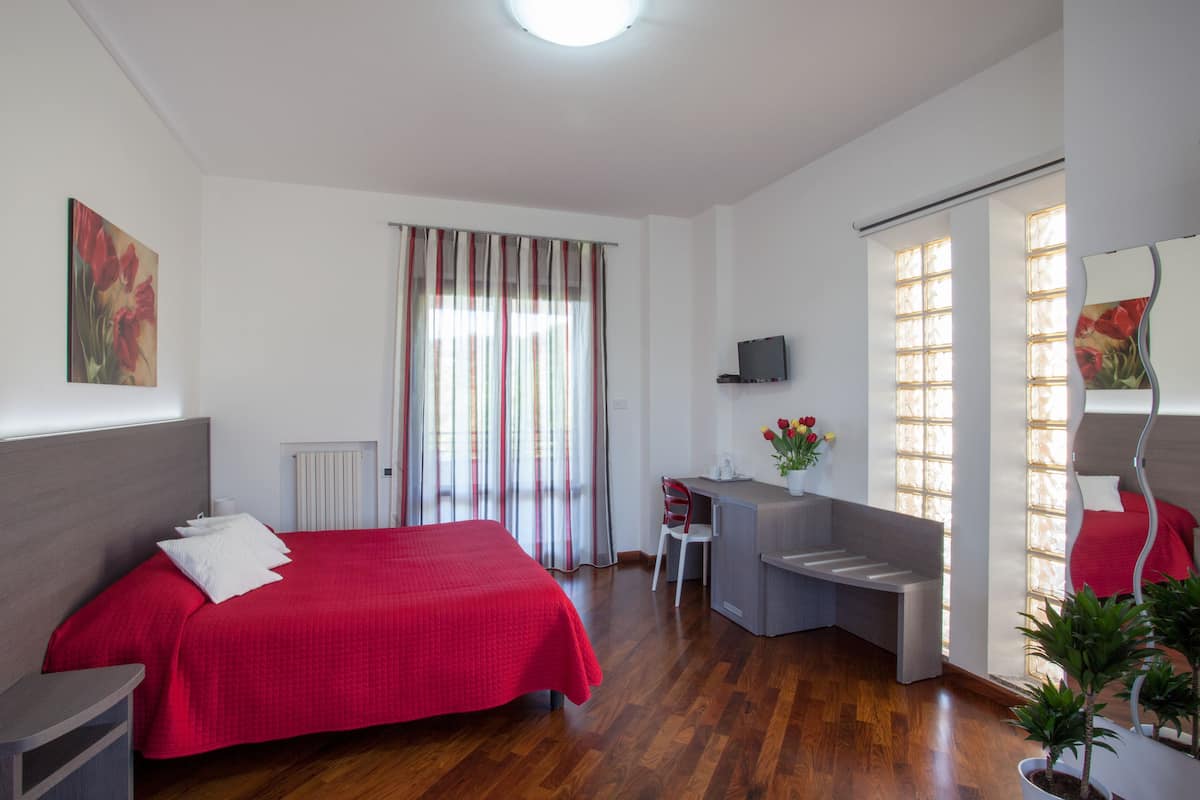 Ein Hotelzimmer mit Bett, Schreibtisch, Stuhl und einem kleinen Balkon.