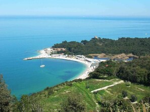 A coastal area with a beach, a small boat, and a path leading to a hilltop with buildings. - Fiori Del Conero (Ancona)