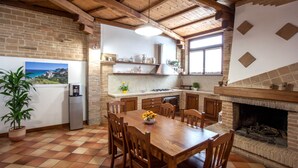 Una cocina con una mesa de madera, sillas, una chimenea de ladrillo y una ventana con vista al mar.