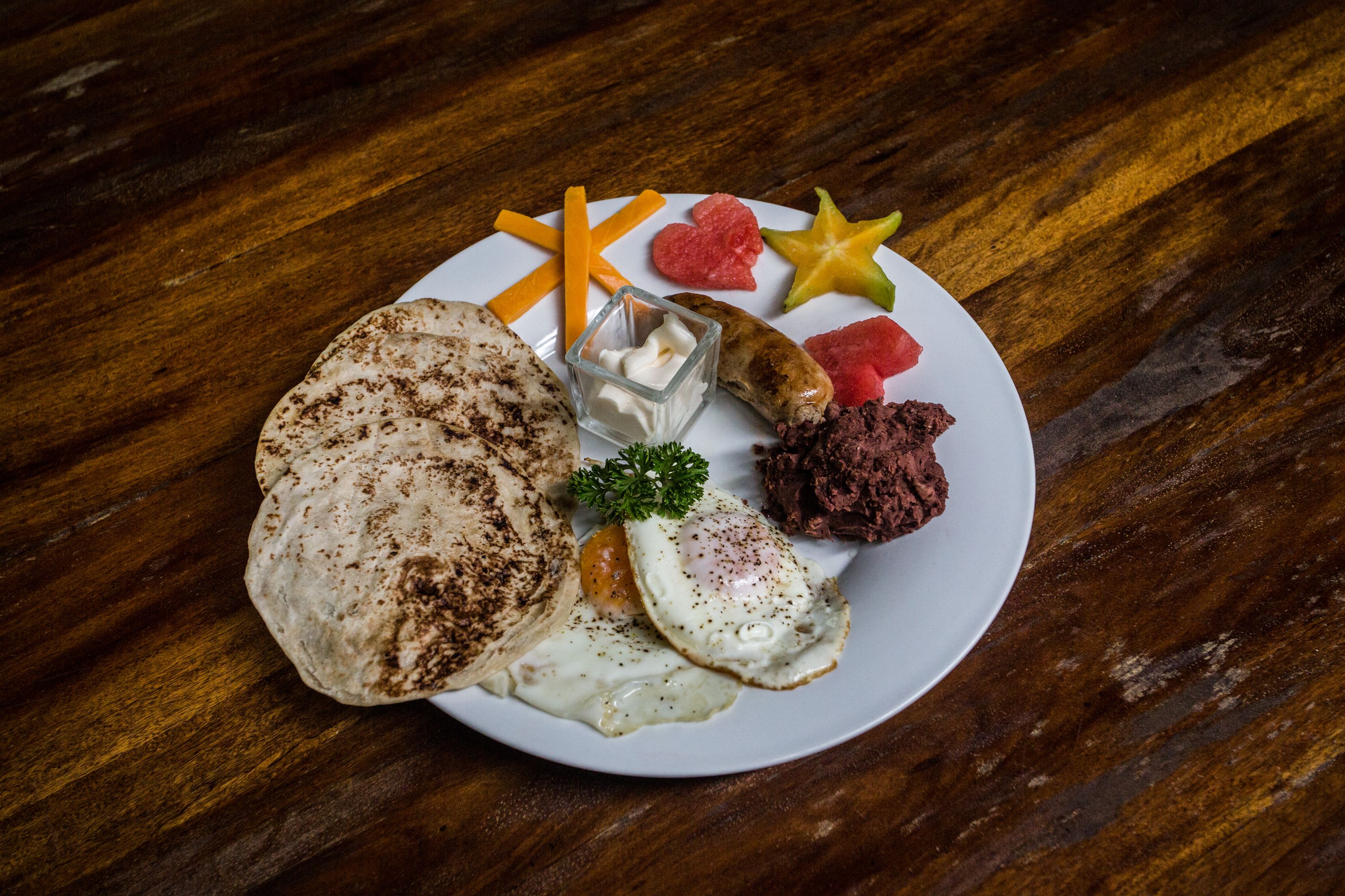 A plate with a grilled patty, two fried eggs, a sausage, a slice of watermelon, a piece of cornbread, and some carrots.