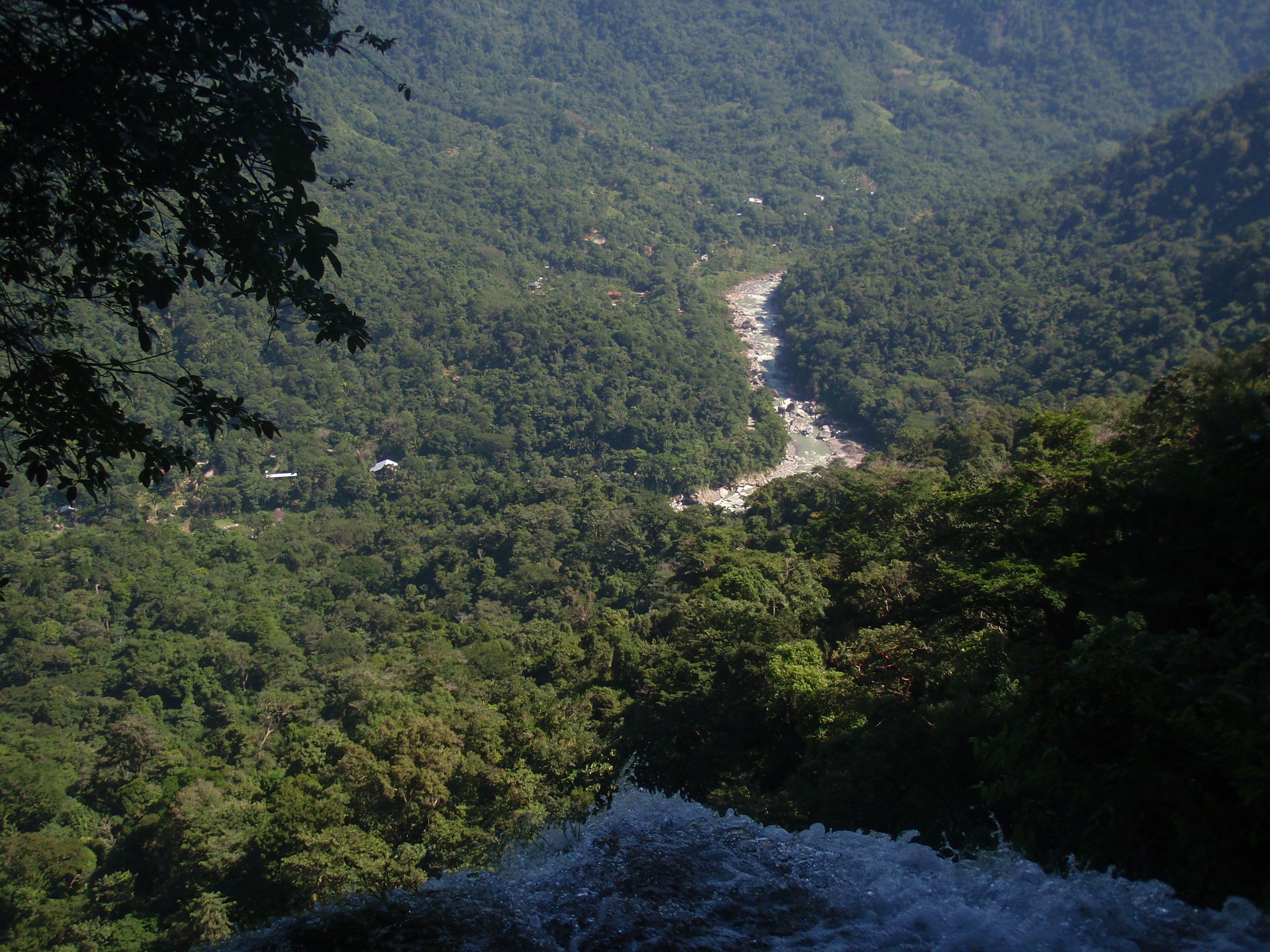 Un río serpentea por un valle densamente arbolado con una cascada al frente.