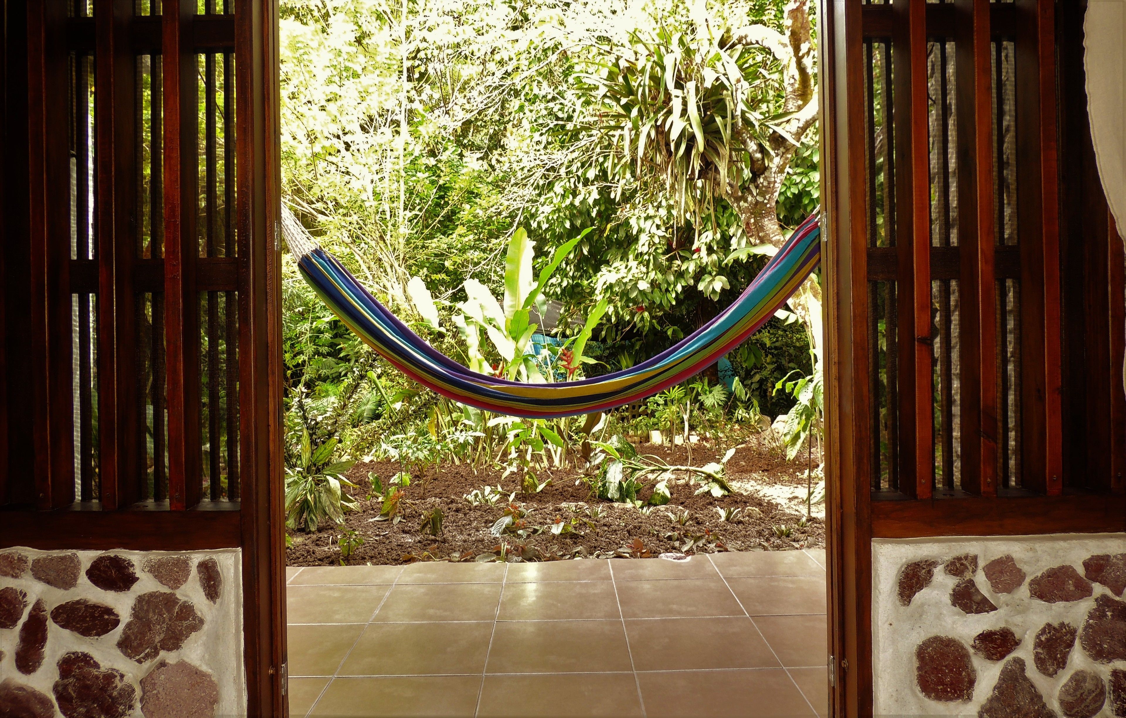 A doorway with a hammock hanging in the center, leading to a garden with various plants and a tiled floor.