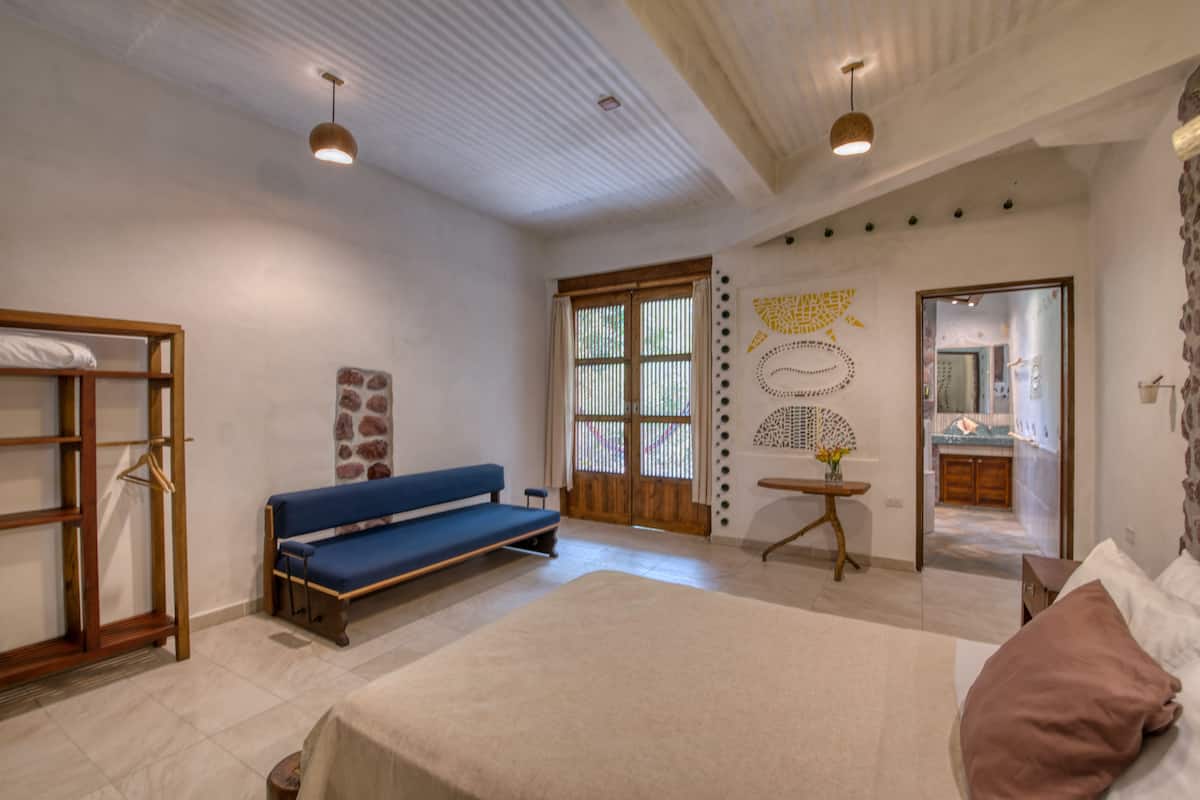 A bedroom with a bed, a bench, a small table, and a mirror.