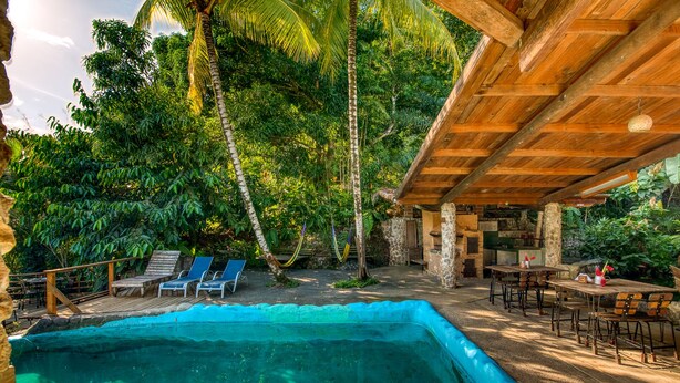 A pool area with lounge chairs, a wooden deck, and a stone wall.