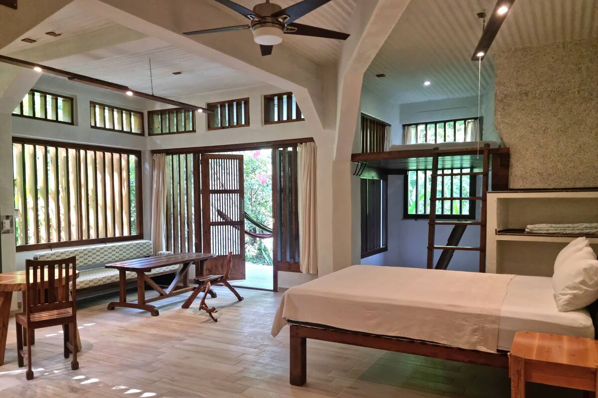 A spacious room with a bed, wooden furniture, and large windows.