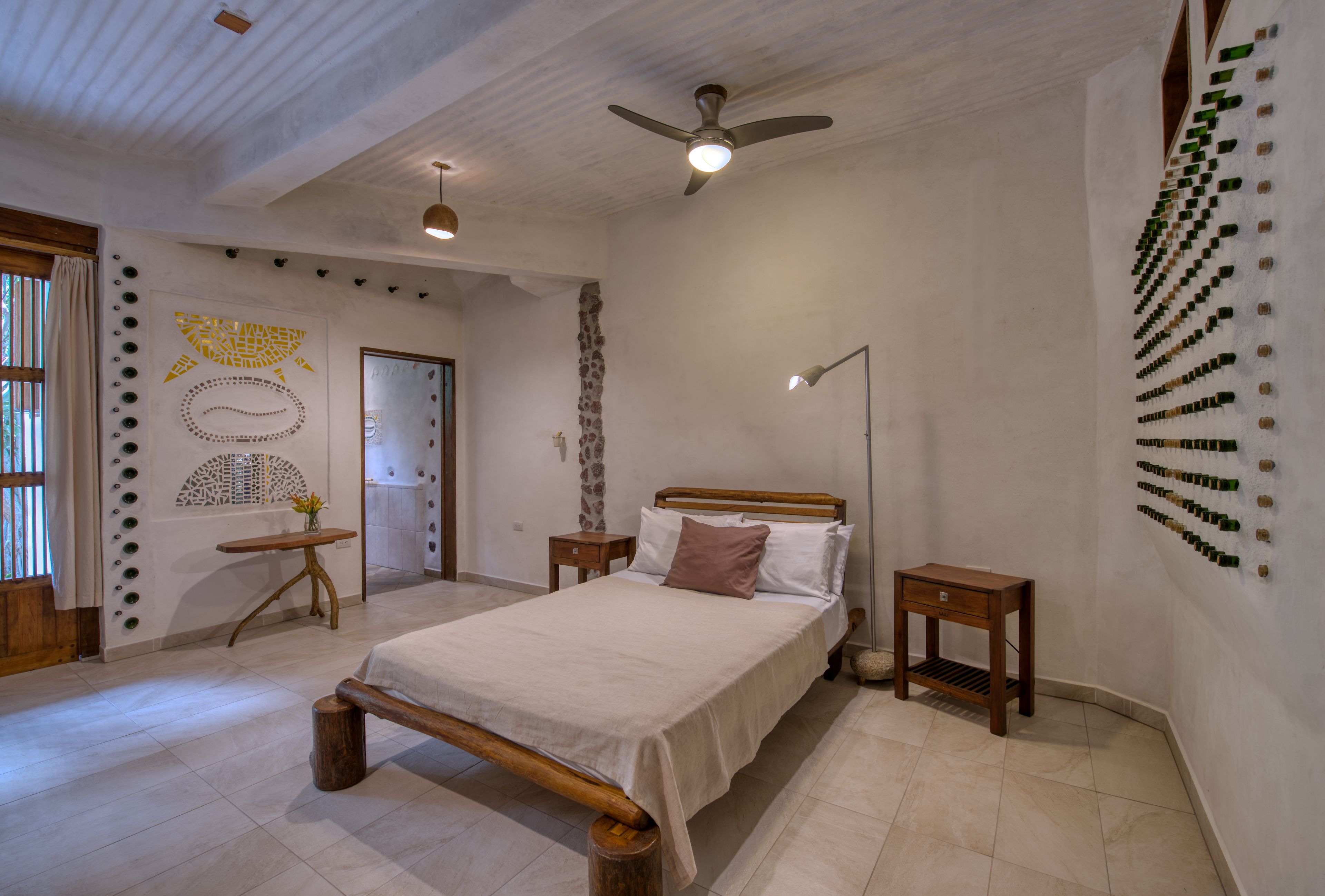 A bedroom with a wooden bed, a ceiling fan, a nightstand, and a wall-mounted bottle holder.