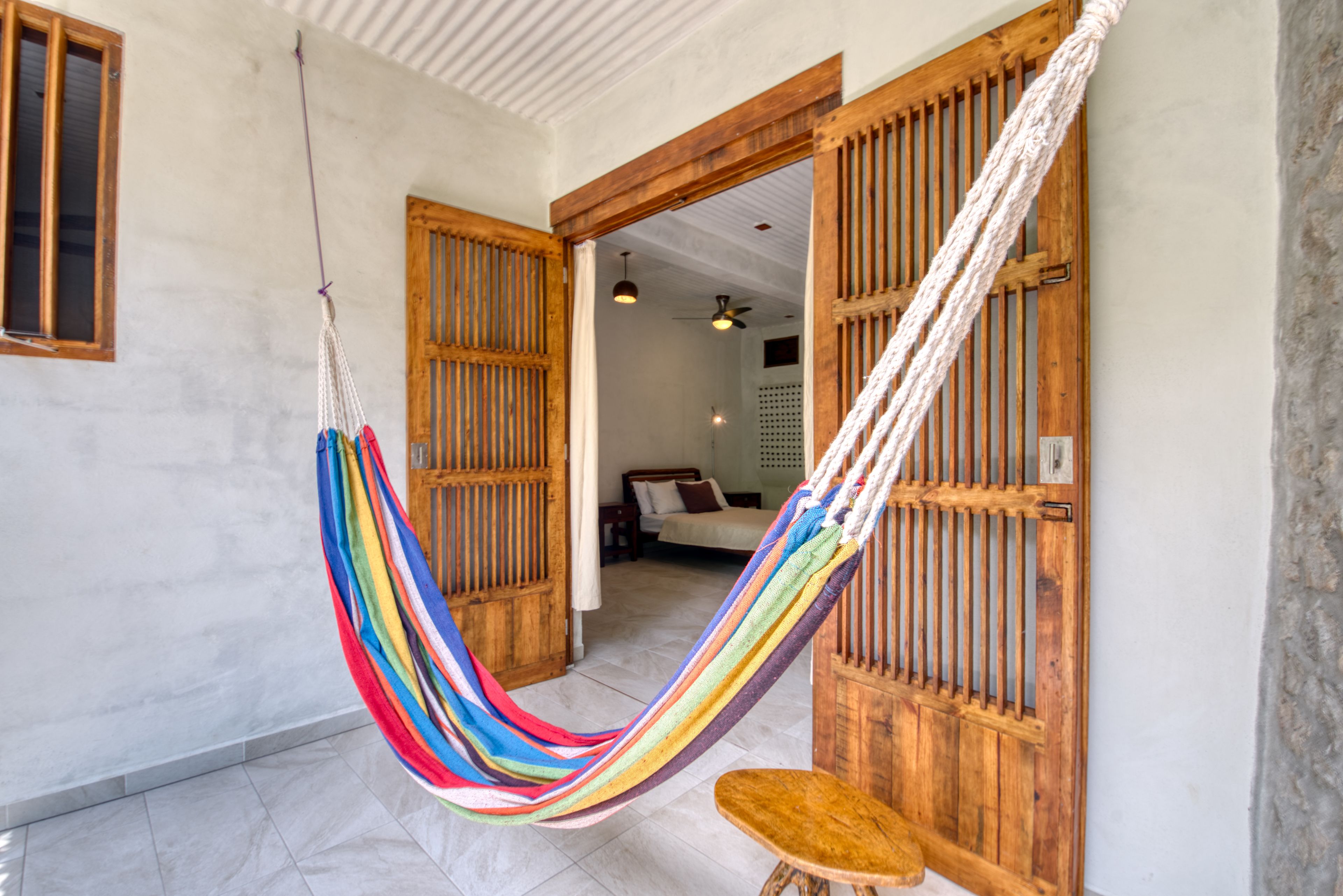 A room with a hammock, wooden doors, a bed, and a ceiling fan.