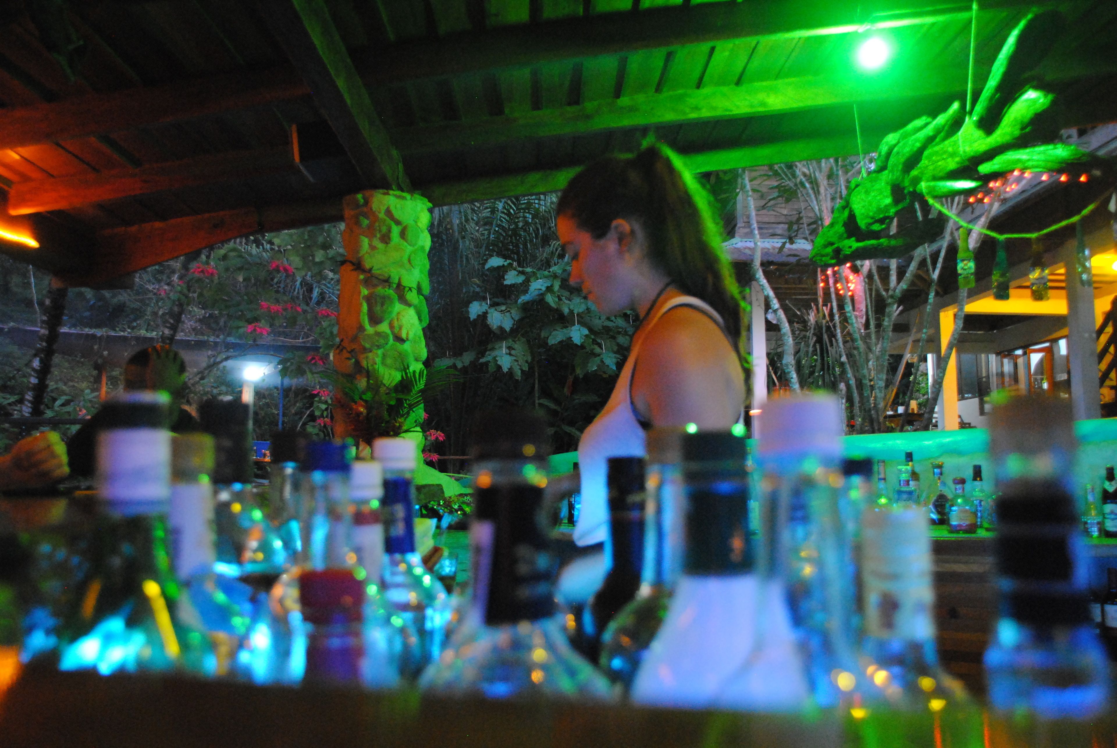 Zona de bar con botellas y una persona al fondo.