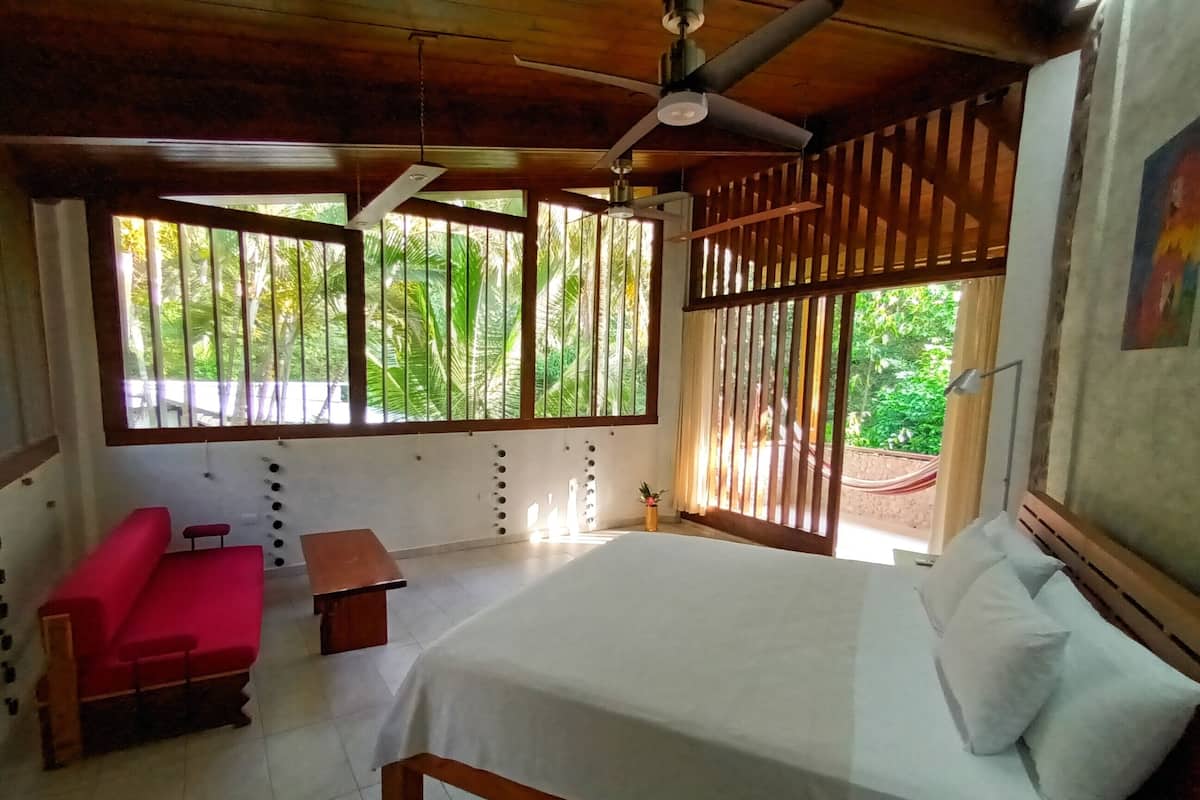 A room with a bed, a red sofa, a small table, and a ceiling fan.