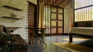 A room with a bed, a sofa, a table, and a view through a bamboo screen door.