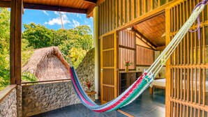 A hammock suspended between a stone wall and a wooden door, with a thatched roof visible outside.