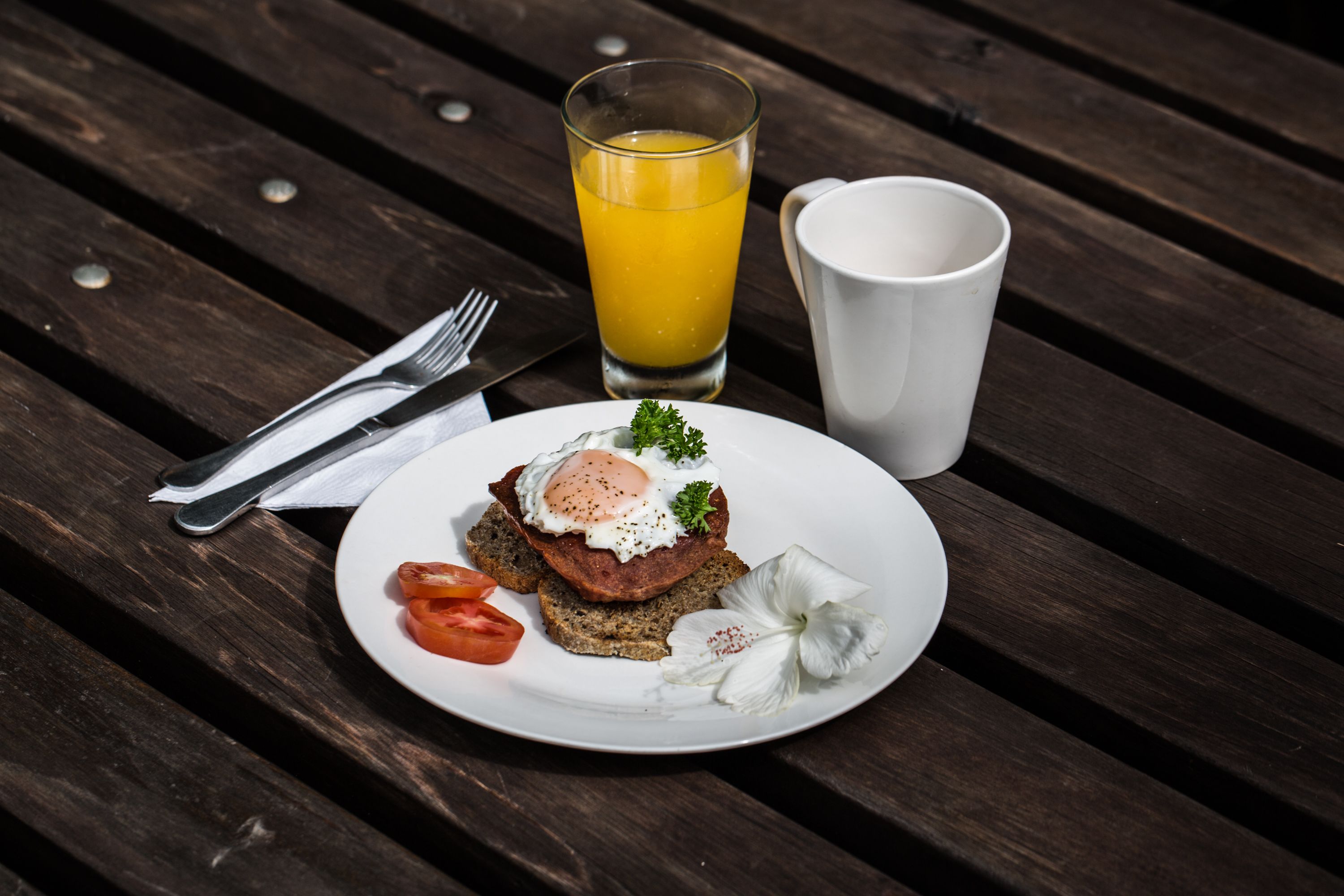 A breakfast plate with toast, egg, tomato, and a white flower on a wooden table.