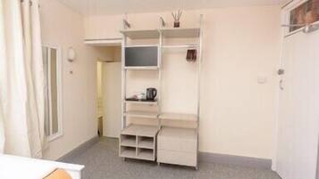 A compact hotel room with a built-in wardrobe, a small seating area, and a kitchenette.