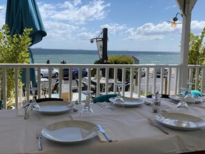 An outdoor dining area with tables set for two, overlooking the sea.