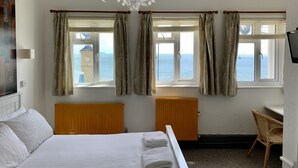 A hotel room with a bed, two windows with curtains, a wooden headboard, a wooden desk, a chair, and a television. - The Waterfront Inn (Shanklin)